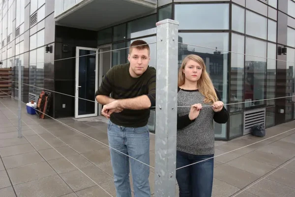 Erin McFadzen and her boyfriend, Erik Clancy, pose for a photo behind a wire fence on their terrace. Photo credit Brigitte Stelzer